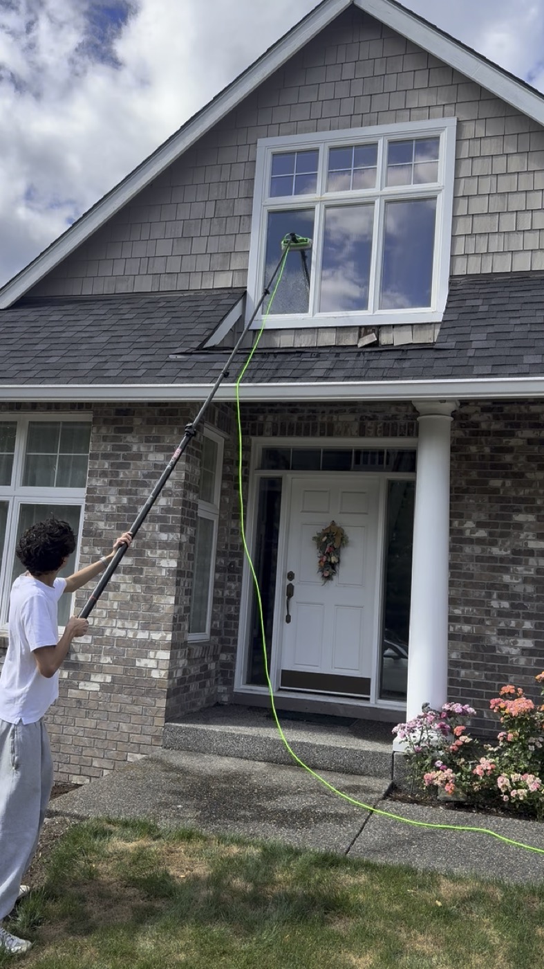Window washing technician cleaning upper windows on brick home in Portland